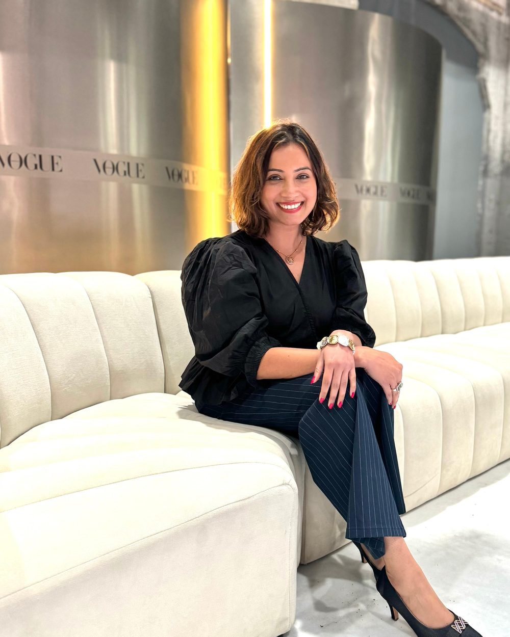 Dipali, founder of Harmony Moments, seated on a cream lounge and smiling warmly