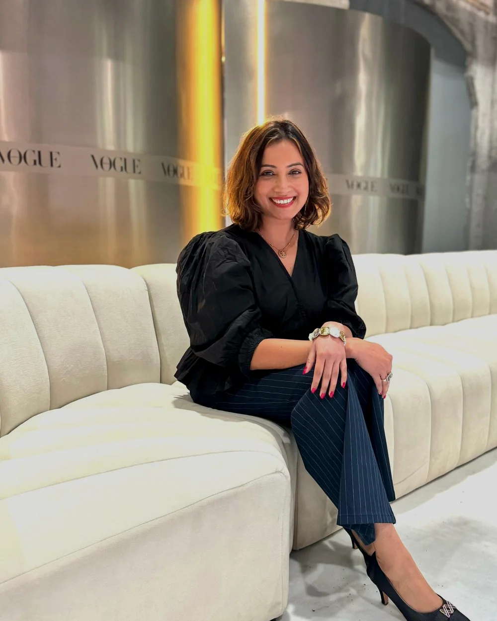 Dipali, founder of Harmony Moments, seated on a cream lounge and smiling warmly