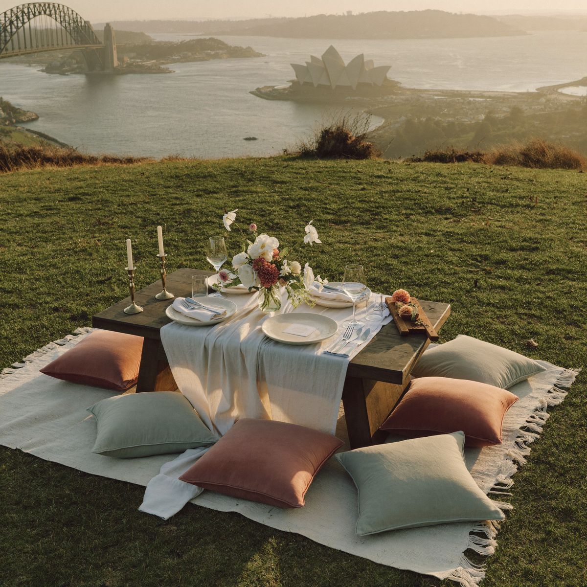 Styled picnic on a grassy headland with Sydney Opera House and Harbour Bridge in the golden distance