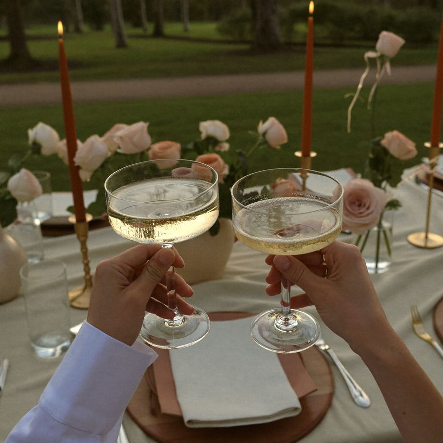 Champagne glasses raised in a toast over a styled anniversary picnic