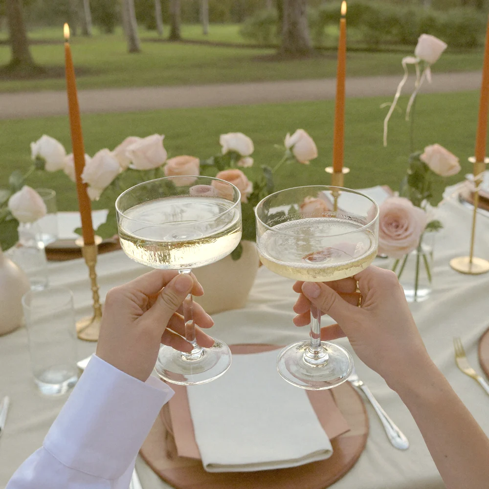 Champagne glasses raised in a toast over a styled anniversary picnic
